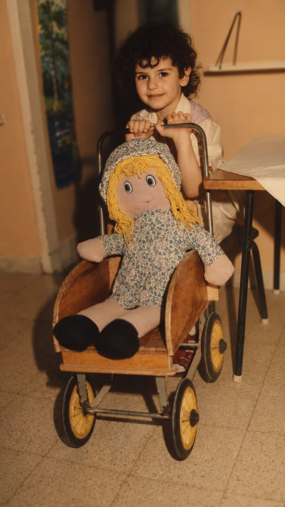 ילדה קטנה עם בובת בד בעגלת עץ ישנה